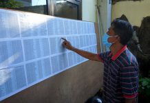 salah satu warga mengecek namanya didaftar penerima bantuan covid -19 yang dipublikasikan melalui papan pengumuman disetiap kelurahan