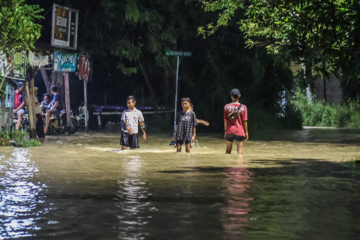 Sekumpulan Anak-anak tengah melintasi banjir yang tingginya mencapai satu lutut anak-anak di Kampung Tengger