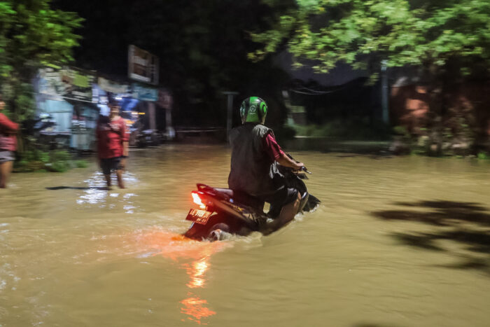 Seorang pengendara sepeda motor melintasi genangan air